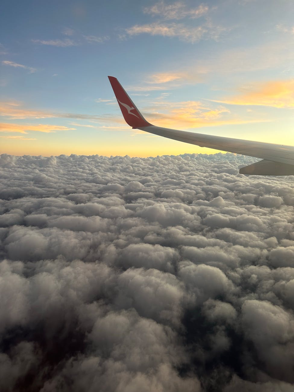 airplane wing over puffy clouds at sunset